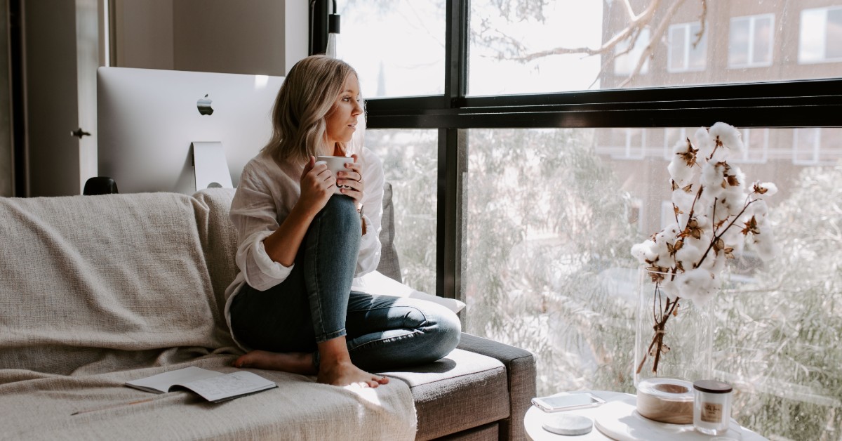 girl with mental illness looking out of a window drinking coffee