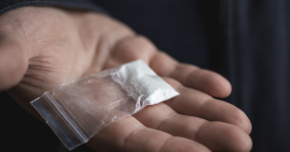 An outstretched hand holding a small bag of cocaine