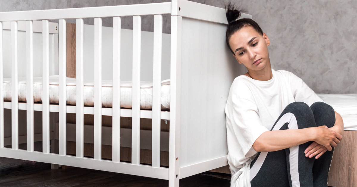 A mother leaning against a crib while clearly displeased