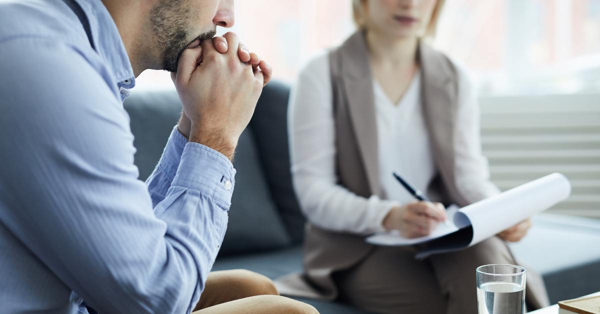 A man sitting across from a woman with a notepad. He seems concerned while she appears to be very attentive.