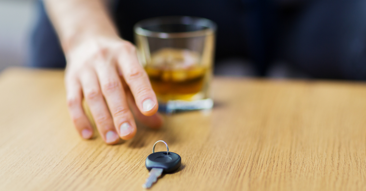 A hand reaches for car keys while a half-filled whisky glass is out of focus in the background 