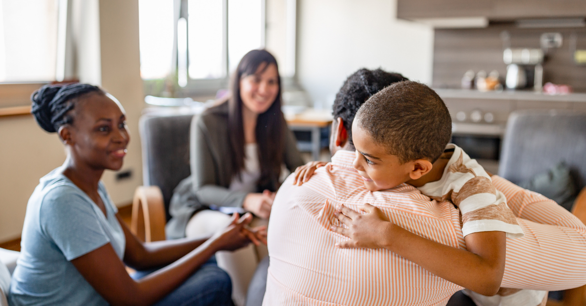 A family sitting close together. The youngest boy is hugging his father while the mother and older daughter look on smiling